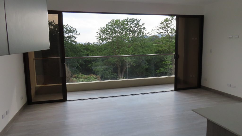 Las puertas corredizas abiertas en el mismo apartamento. El piso es gris, la vista es verde, bosque. Las puertas están abiertas y se ve la vista.
